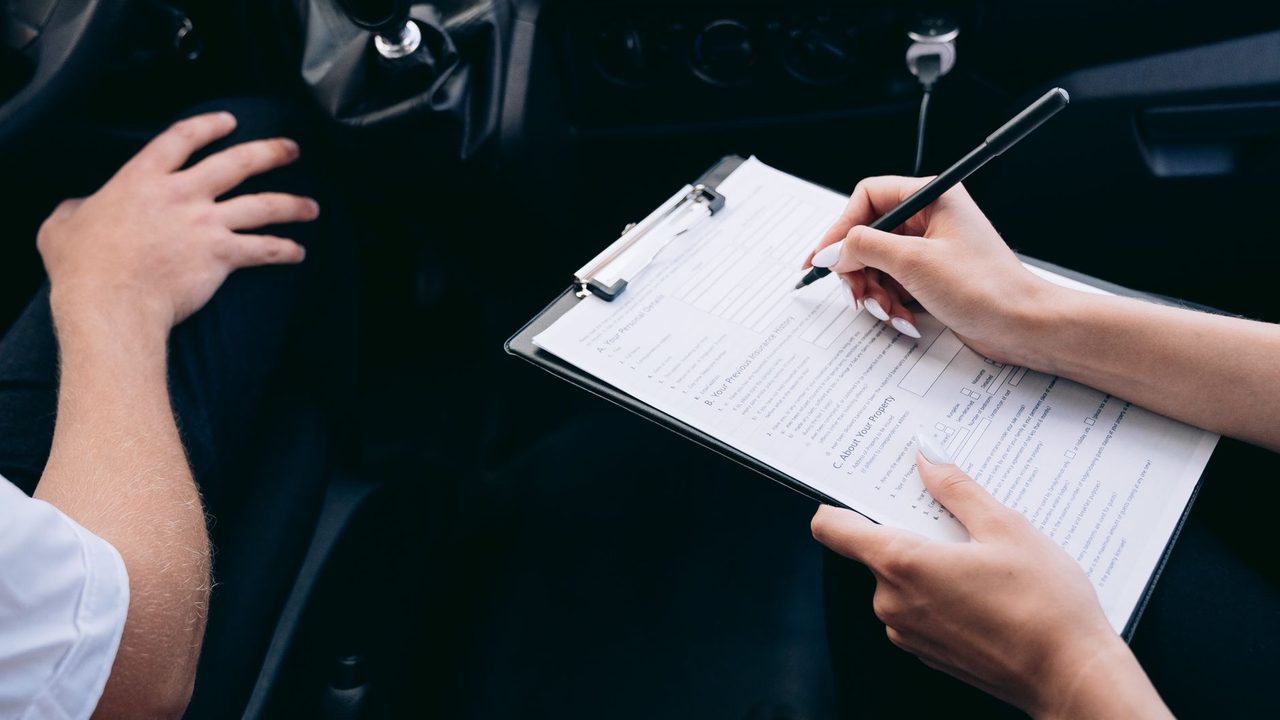 Dos personas dentro de un auto firmando un formulario sujeto a un portapapeles