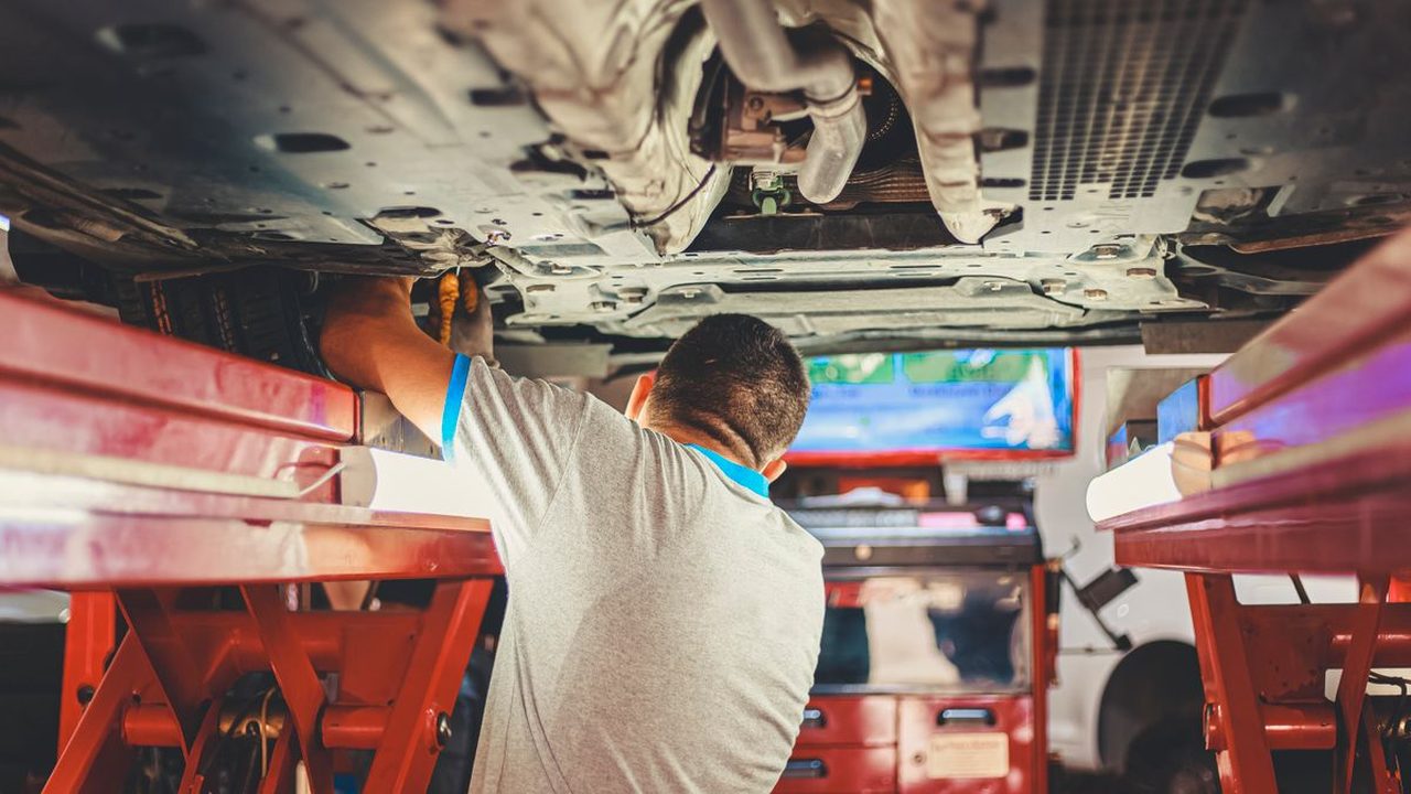 Mecánico revisando los bajos de un auto elevado sobre una rampa de taller